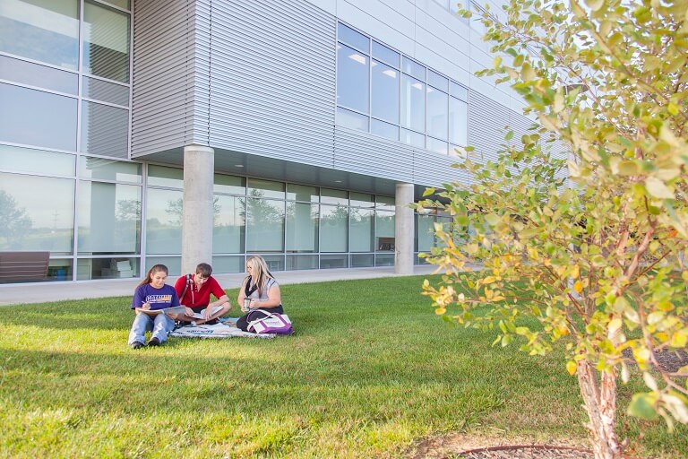 Three students sitting outside a campus building on the lawn