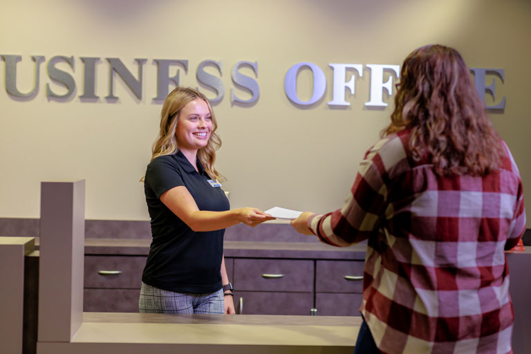 student handing document to staff at the Business Office