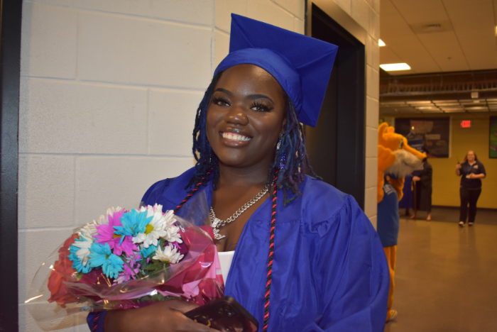 student wearing graduation attire and holding a bouquet of flowers