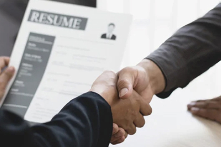 two hands in a hand shake over a resume